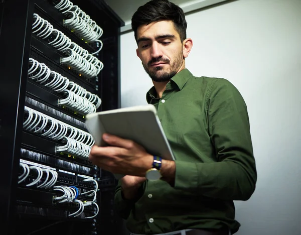 Engineer man, cable and server room with a tablet for programming, maintenance and software upgrade. Young male technician person with technology in data center for wire, hardware and internet.