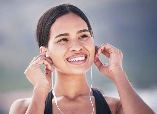 Fitness, smile and woman with music earphones outdoor for running, training and sports routine on blurred background. Exercise, podcast and happy female runner with radio, track and audio motivation.