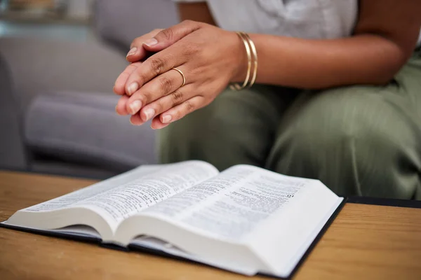 Hands, bible and woman in prayer in home, lounge and reading book of faith, religion and worship study for mindfulness. Person, praying and studying holy book for peace, praise and meditation.