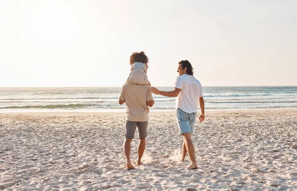 Beach, LGBT and walking kid, family and enjoy freedom together on travel vacation, holiday or nature freedom. Love, back and gay couple, people or parents bonding with adoption child on shoulder.