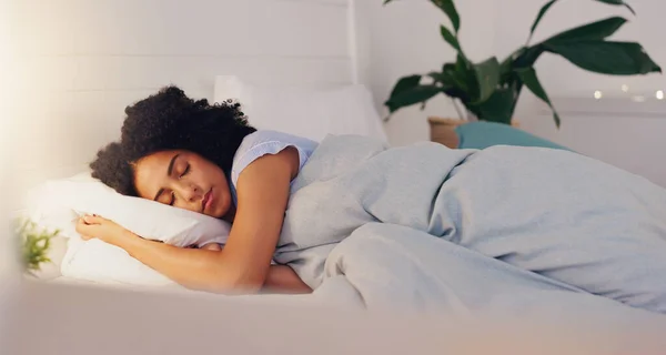 Young black woman sleeping in bed in her bedroom while resting and having a dream at home. Relax, peaceful and calm African girl taking a nap with a comfortable pillow and blanket at her house