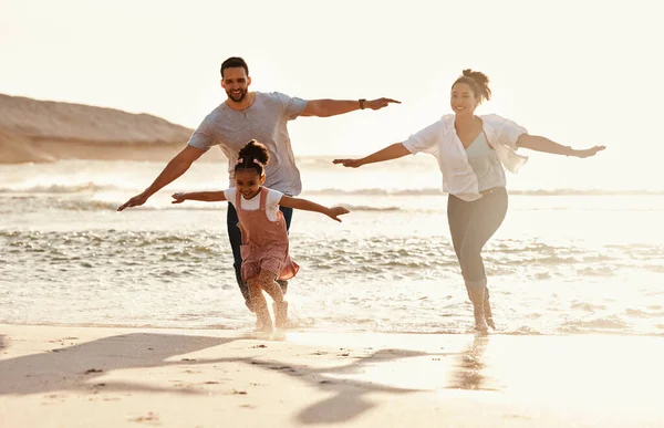 Family, running in ocean and freedom on beach with sunshine, fun together with games and bonding on vacation. Travel, adventure and playful, parents and child with happy people in nature and energy.