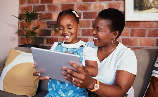 Happy, African mom and girl on tablet in home, living room and lounge with online education, games and learning technology. Streaming, mobile app or mother and child relax with social media on sofa.