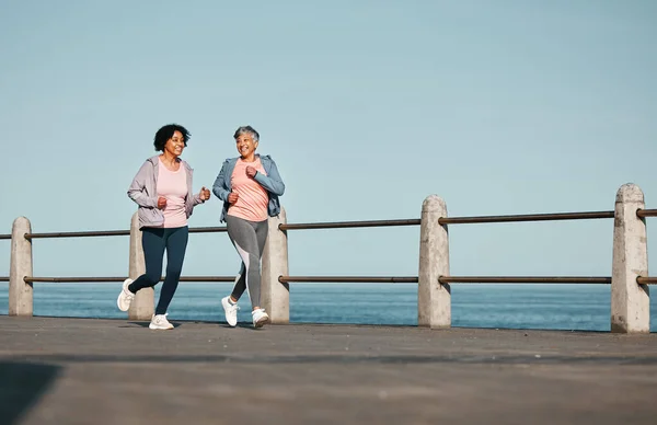 Senior women, fitness and running at beach for health, wellness and exercise in nature together. Elderly, friends and ladies at sea talking, workout and active retirement, fun and bonding ocean run.