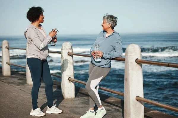 Fitness, walking and senior women relax by ocean for healthy lifestyle, wellness and cardio on promenade. Sports, friends and female people talking on boardwalk for exercise, training and workout.