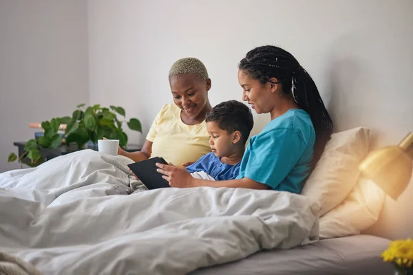 Child, LGBT family and tablet in bed with internet in home bedroom for learning and education. Adoption, lesbian or gay women or parents with a foster kid and technology for online games or video.
