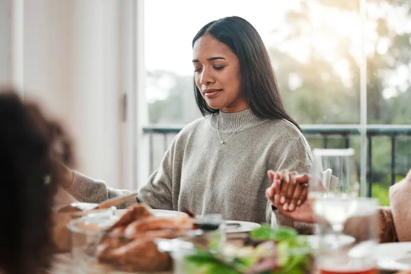 Woman, praying and holding hands at family dinner at thanksgiving celebration at home. Food, female person and eyes closed at a table with religion, lunch and social gathering on holiday in house.