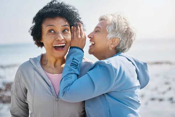 Gossip, beach and senior friends with a secret, whisper or talking in ear for a funny joke after outdoor exercise. Laughing, crazy and elderly women listening to conversation or story at the sea.
