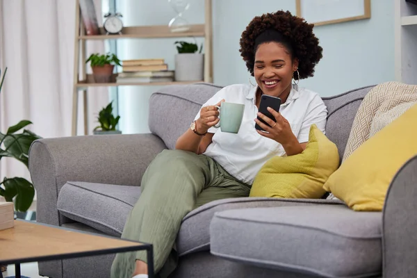 Woman, coffee and smartphone on sofa in living room, social media and reading funny memes. Happy female person relax on couch, cellphone and tea for texting, chat app and download mobile games.