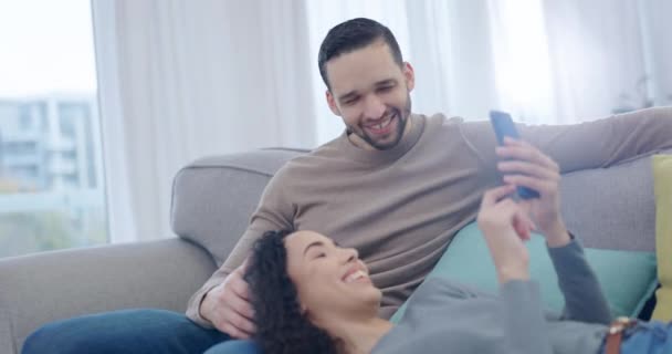 情侣们 在家里客厅的沙发上 在电话笑话中谈笑风生 放松地阅读博客 社交媒体和有趣的迷因 快乐的男人 女人和科技应用程序 用于观看喜剧 结合和爱情 — 图库视频影像