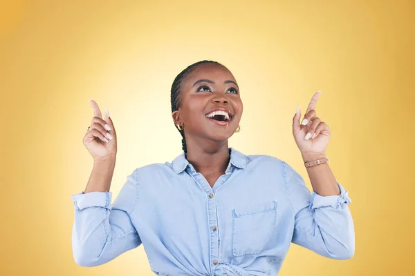 Black woman, excited and surprise, pointing up and advertising with presentation news isolated on yellow background. Announcement, opportunity and offer with wow, communication and ads in studio.