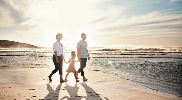 Beach, sunset and family holding hands, walking and bond, relax and happy on vacation in nature together. Travel, love and girl chid with parents at ocean with freedom, adventure or journey in Bali.