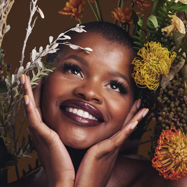 African woman, plants and thinking for aesthetic in studio with flowers for beauty, wellness and glow by brown background. Girl, model and smile on face for idea, leaves or memory with skin cosmetics.
