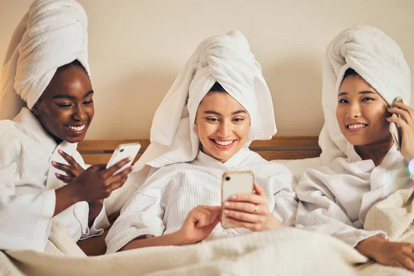 Spa day, sleepover and friends with phone in bed relax with social media during beauty routine at home. Happy, self care and women in bedroom with smartphone for internet, search or diy skincare idea.