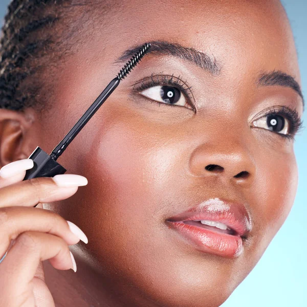 Studio face, black woman and eyebrow mascara, product or cosmetology tools for facial cosmetics application. Beauty routine, brow care makeup and closeup African person on blue background.