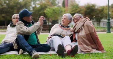 Piknik, park ve yaşlılar anılar, sosyal medya ve fotoğrafçılık için çimlerin üzerinde fotoğraf çekiyorlar. Emeklilik, dostluk ve kameralı yaşlı kadın ve erkekler hafta sonları rahatlayıp eğleniyorlar..