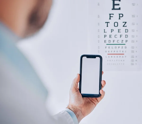携帯電話 および目の検査の人の手 モバイルアプリやインターネットでビジョンのためのテストまたは予約評価 携帯電話 モックアップおよびオプトメトリック医師は技術のオフィスで視力をテストします — ストック写真