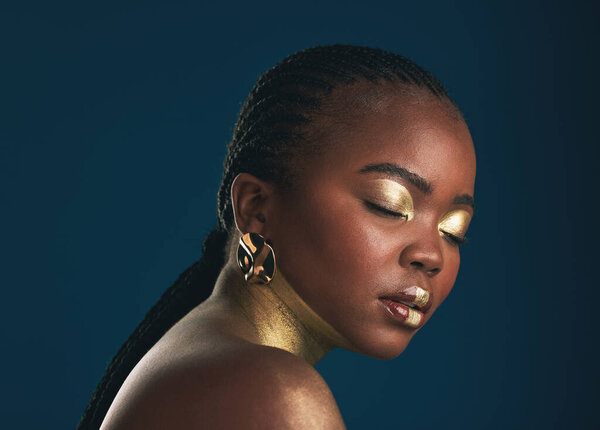 Gold makeup, studio face and black woman relax with creative art, facial cosmetics paint and beauty. African culture, color and person with eyes closed, wellness and creativity on blue background.