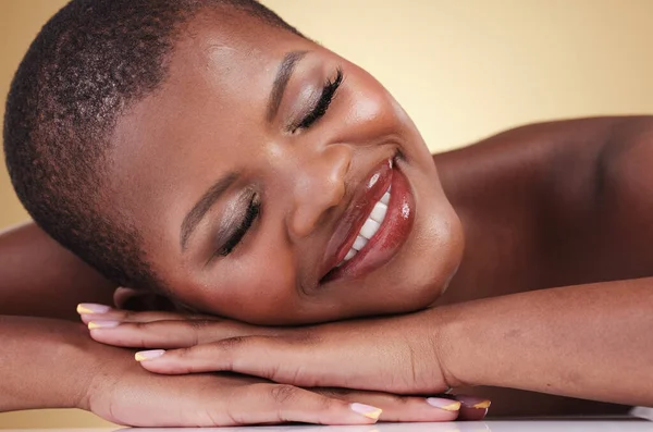 Skin, beauty and makeup of a black woman in studio for self care, glow or cosmetics. Face of African aesthetic model person with facial shine, dermatology and head on hands on beige background.