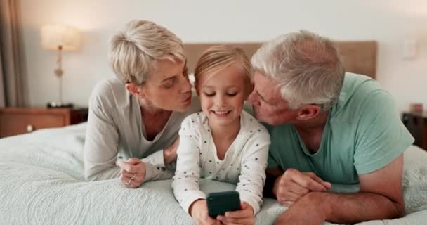 游戏和祖父母亲吻一个女孩在家里的床上玩或结合 孩子或与老年男女一起在卧室里用手机爱着孙女的家庭 — 图库视频影像