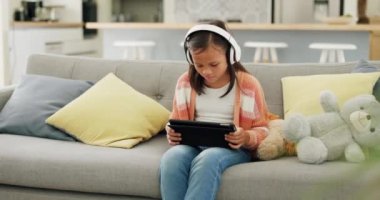 Tablet, müzik ve kardeş çocuklar evlerinin oturma odasındaki kanepede uzaktan eğitim ya da oyun için beraberler. Teknoloji, aile ve öğrenim kız çocuklarla bir oyun oynarken bağ kurmak..