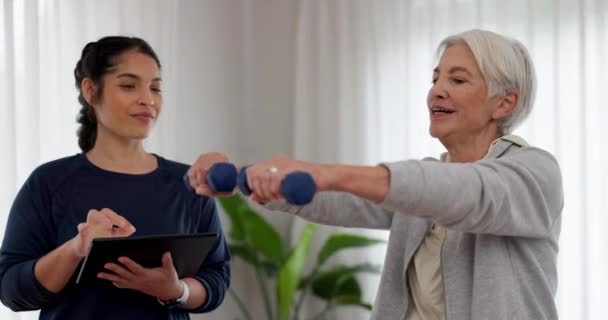 シニア女性の理学療法 コンサルテーション フィットネス試験のためのダンベル古いタブレット またはリハビリテーションの進捗状況を追跡する 身体療法 退職および理学療法士は 腕の運動を有する患者をサポートします — ストック動画
