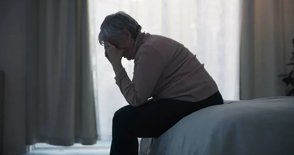 Stress, depression and sad old woman in bedroom with anxiety, mental health problem and debt in retirement. Lonely senior female person crying at home for headache, pain and fatigue of crisis in mind.