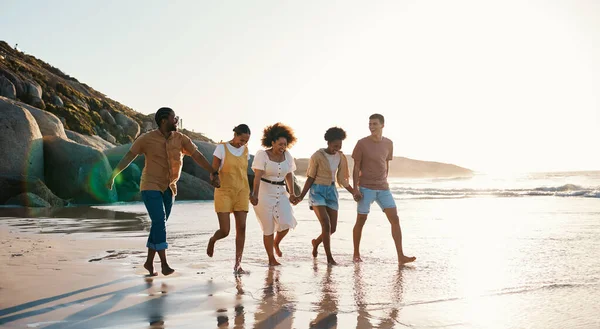 Summer, friends and people happy at sunset beach for fun, holding hands and travel with love. Diversity, men and women group in nature with sand, freedom and happiness on a vacation or holiday.
