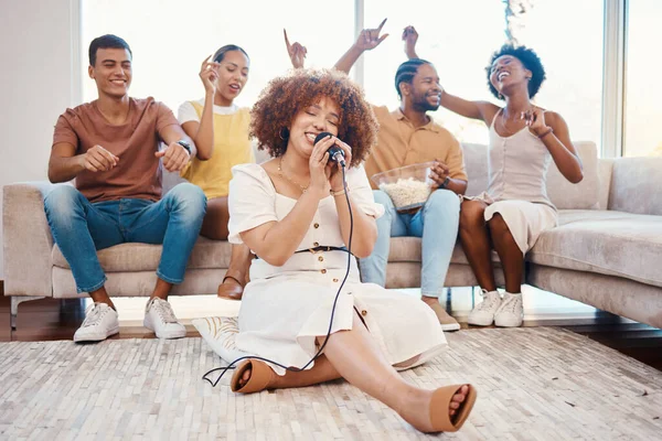 Microphone, friends or happy woman singing in home living room together in party on holiday vacation break. Girl singer, men or group of funny women laughing in a fun karaoke game with popcorn snacks.