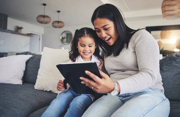 Tablet, surprise and a mother on the sofa with her daughter in the living room of their home together. Wow, family or children with a mother and girl looking at social media or a good news email.