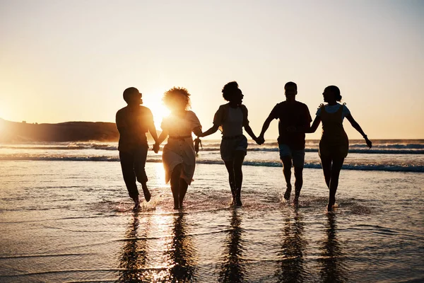 Holding hands, silhouette and friends at the beach with freedom, fun and bonding at sunset. Ocean, shadow and group of people at the sea for travel, adventure and journey in sea trip in Los Angeles.