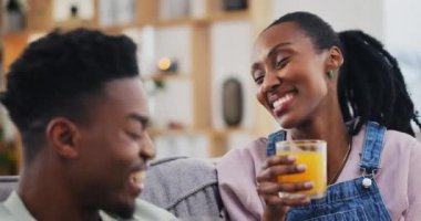 Mutlu, siyah çift ve portakal suyu evde oturma odasında kanepede sağlıklı beslenme, beslenme ve sağlıkta. Afrikalı erkek, kadın ve cam içinde meyve, organik C vitamini ve komik vejetaryen gülüşü..