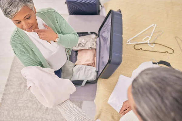 Mature couple, clothes and packing suitcase in home for travel, vacation or holiday in top view. Man, woman and prepare luggage in house, thinking and choice decision on planning journey in bedroom.