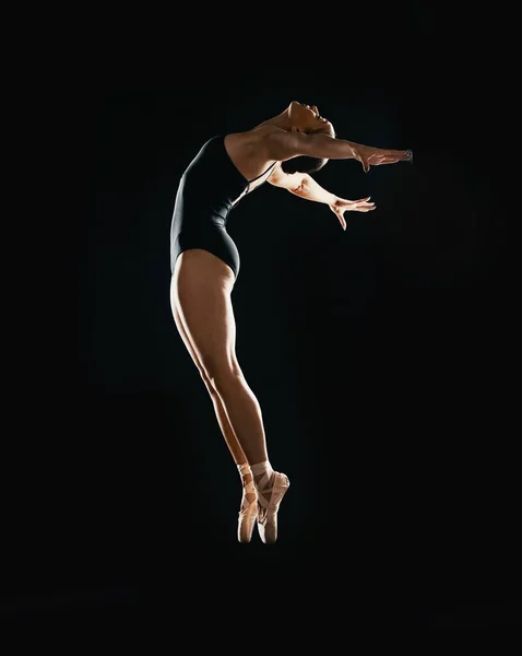 Art, ballet jumping and woman on black background in dance performance with balance, action and talent. Dark aesthetic, flexible ballerina or dancer training with fitness, creativity and studio show