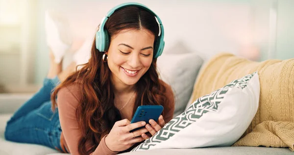 Girl, phone and music on sofa to relax with headphones with smile, typing and happy on social media. Woman, smartphone and streaming song on internet while reading communication, blog post or email.