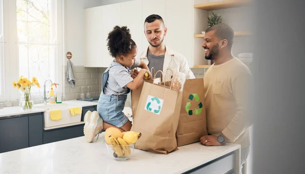 Recycling, blended family or adoption with a daughter and gay couple in the home kitchen for sustainability. LGBT, eco friendly or waste with a girl and parents unpacking bananas from a grocery bag.