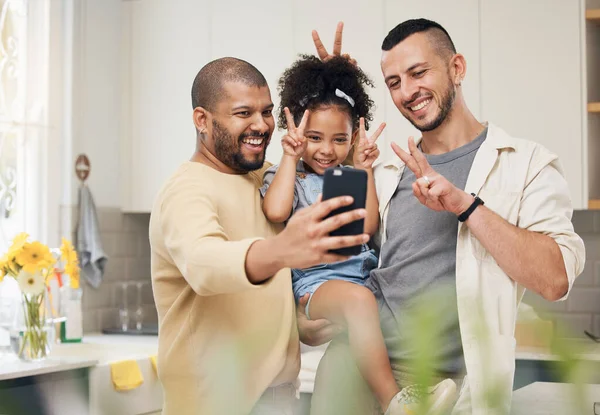 Selfie, blended family and a happy girl with her gay parents in the kitchen together for a profile picture. Adoption photograph, smile or love and a playful daughter with her lgbt father in the home.