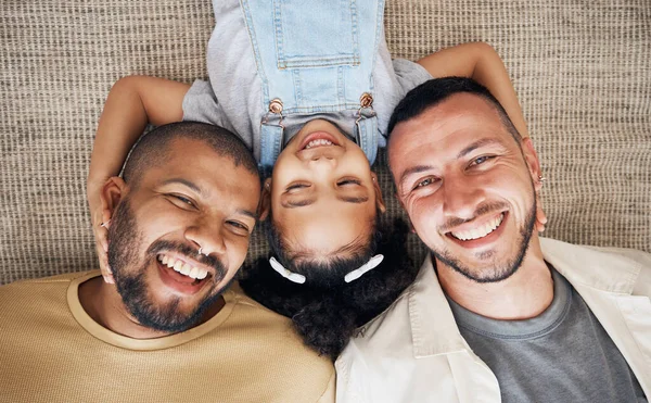 Gay dad, blended family and foster with a girl lying together on the floor of the home for adoption from above. LGBT love, children or kids and a daughter bonding with her happy parents in the house.