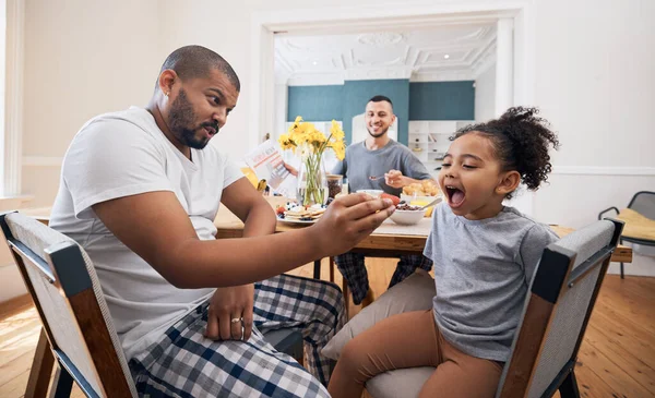 Gay couple, breakfast and father feeding child meal, food or morning cereal for youth development in home dining room. Family bond, adoption or homosexual dad smile for hungry kid girl eating.