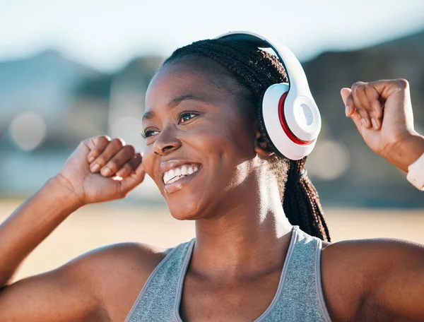 Black woman, smile and headphones, music and fitness outdoor with running, race and athlete, wellness and sport. Happy runner, audio streaming and exercise with workout, health and training for race.