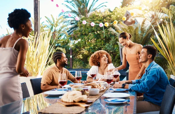 Happy people, friends and food outdoor on a table for social gathering, happiness and holiday celebration. Diversity, men and women group eating lunch at party or event with wine to relax in garden.