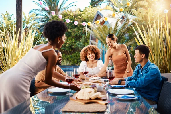 Friends, outdoor and eating food at a table for social gathering, happiness and holiday celebration. Diversity, men and women group at lunch, party or reunion with wine in a garden for fun and relax.