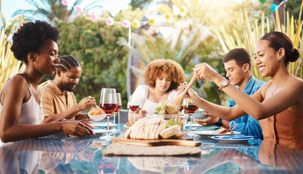 Friends at lunch, party in garden and happy event with diversity, food and wine for bonding together. Outdoor dinner, men and women at table, group of people eating with drinks in backyard in summer