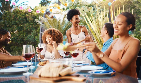 Group of friends at lunch, party in garden with smile, eating and happy event with diversity. Outdoor dinner, men and women at table with food, wine and talking together in backyard with celebration