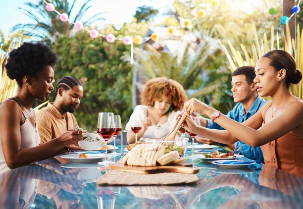 Friends at dinner, party in summer in garden and happy event with diversity, food and wine for bonding together. Outdoor lunch, men and women at table, group of people eating with drinks in backyard.