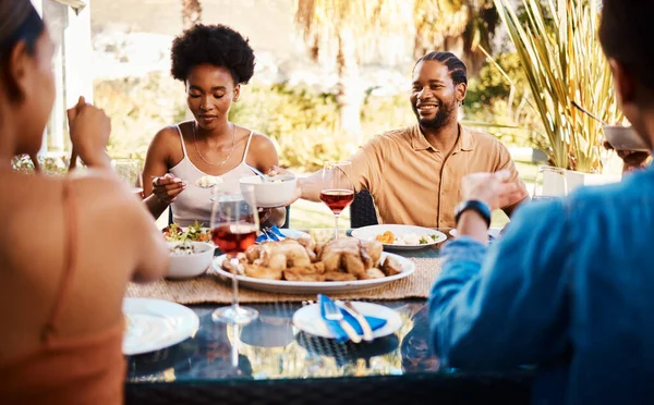 Group of friends at table, eating in garden and happy event with diversity, food and wine bonding together. Outdoor dinner, men and women at lunch, people at party with drinks in backyard in summer