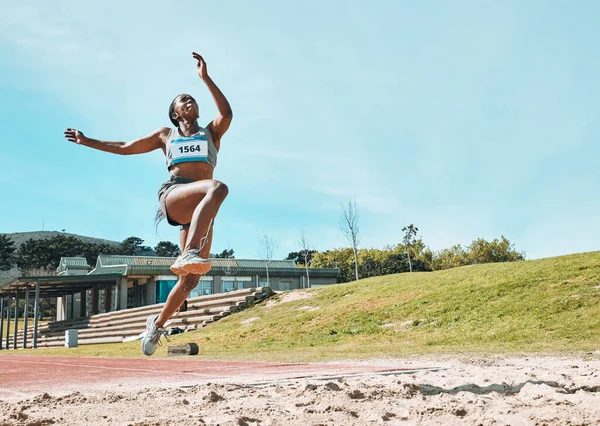 Athletics, fitness and sports woman doing long jump in outdoor competition, athlete challenge or workout. Agility, sand pit and female person training, exercise and action performance at arena event.