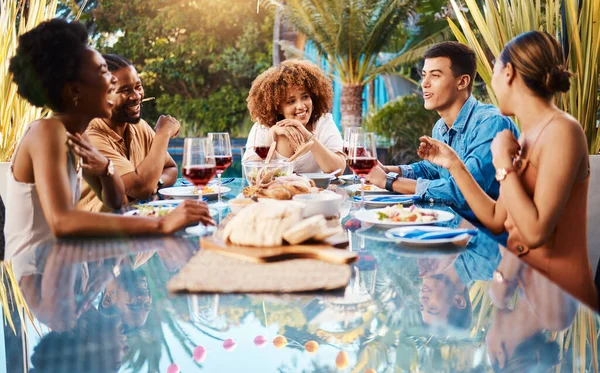 Friends, food and outdoor table for holiday, Christmas or thanksgiving lunch and wine at backyard patio. Young people or social group with alcohol, brunch and drink or talking of summer vacation.