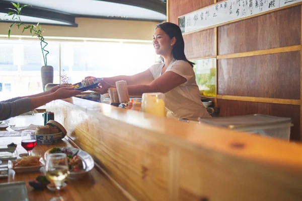 stock image Sushi serving, restaurant chef and woman with smile from food and Asian meal in a kitchen. Happy, female waiter working with lunch order with cooking and hospitality job in Japanese bar with service.