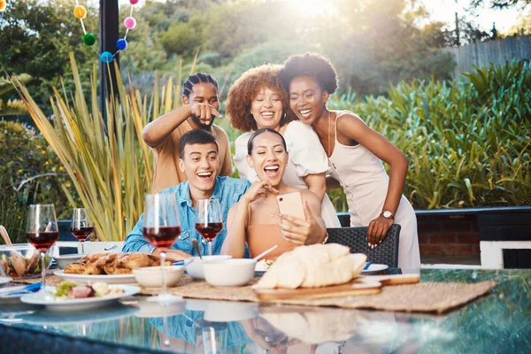 Selfie, group of friends at dinner in garden and happy event with diversity, food and wine at outdoor party. Photography, men and women at table, fun people with drinks in backyard at sunset together.
